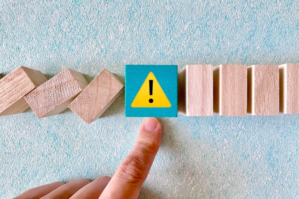 ドミノ倒しを止めて危機回避するイメージ　注意マークとストップする手